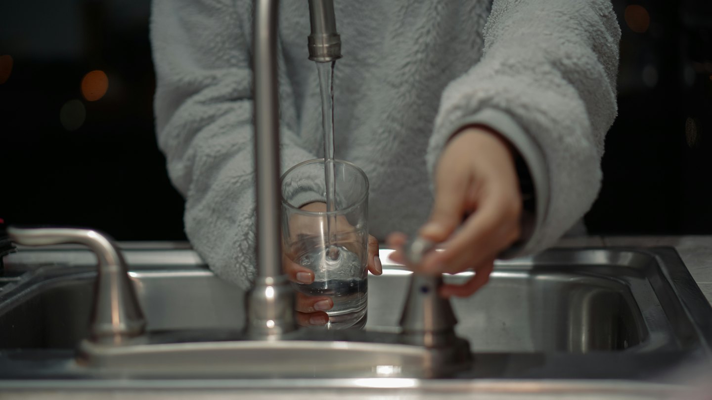 Person in a grey top filling a glass with faucet water.